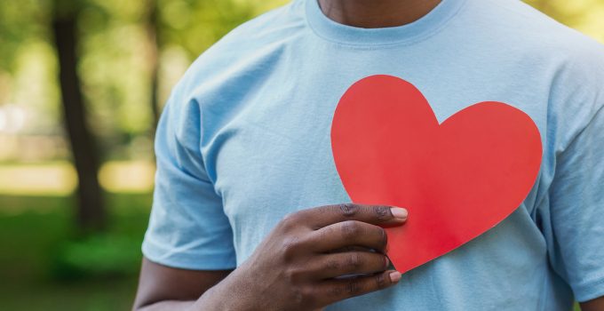 Man in blue t-shirt holding red paper heart to his chest