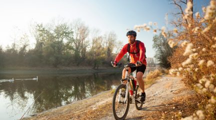 A man wearing a helmet rides a mountain bike along a path next to a river