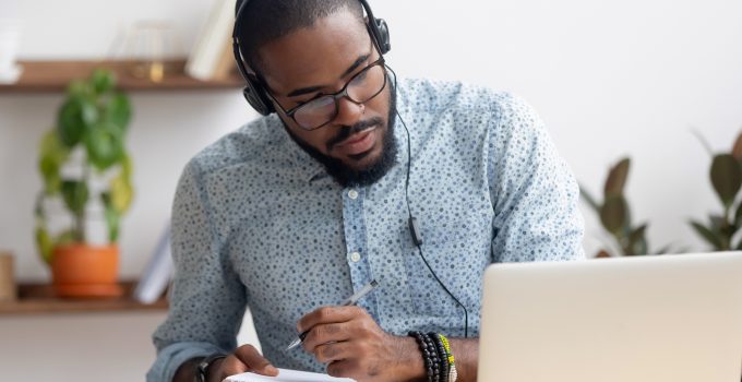 Young man wearing headphones taking notes during an online class