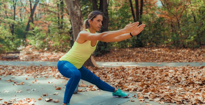 A woman doing side lunges outdoors with autumn leaves around her