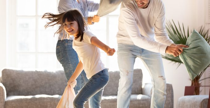 Two parents and a daughter have a pillow fight in the living room
