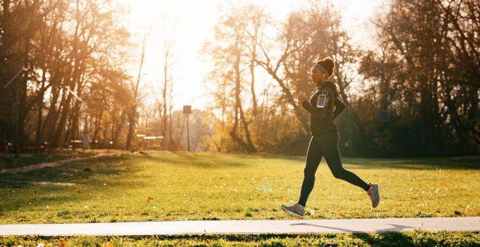 A woman runs through a park in full workout gear and headphones