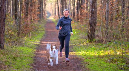 A fit older woman runs through the woods with her dog