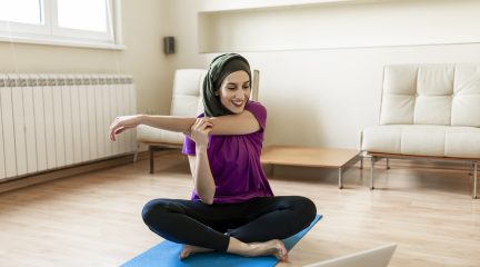 Young muslim woman in a hijab stretching and following an online yoga class