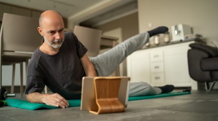 Older man doing yoga at home whilst watching iPad