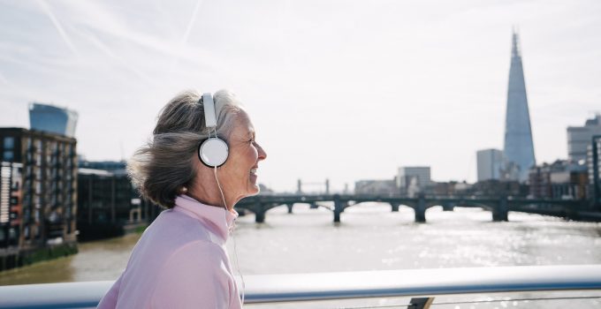 A senior woman running across a bridge in London listening to music