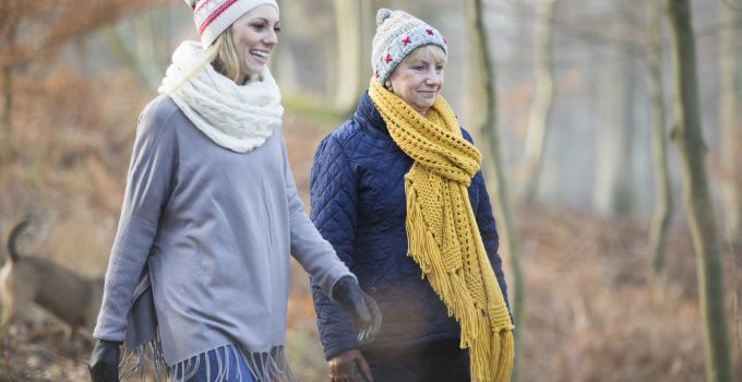 Two women are on a winter walk together in the woods, all wrapped up