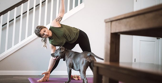 Woman doing yoga in her living room while a large dog stands nearby